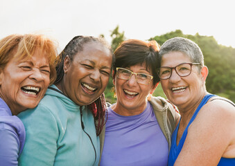 Happy multiracial senior women smiling on camera while hugging each other outdoor - Elderly friendship concept