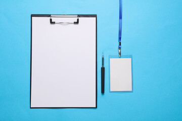 Clipboard with blank sheet of paper, id card on rope, blue background. Template for design. Top...
