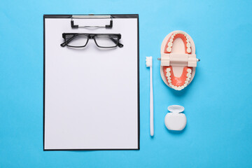 Caring for the oral cavity, a visit to the dentist. Clipboard with jaw, toothbrush and dental floss on blue background. Medicine concept