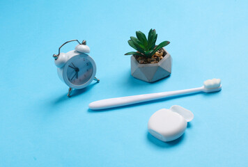 Dental care. Toothbrush with dental floss, alarm clock on blue background