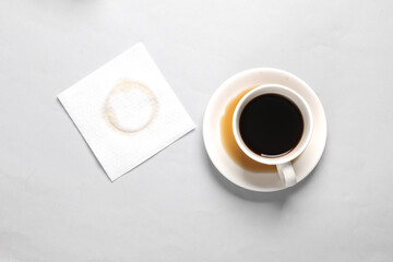 Spilled cup of coffee with napkin on gray background