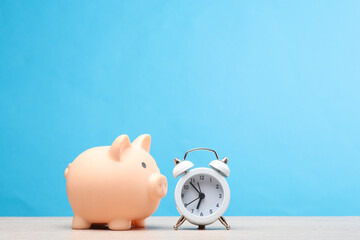 Alarm clock with piggy bank on the table, blue background