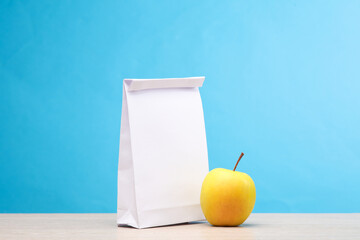 White lunch pack and apple on the table, blue background. Snack to school. Template for design
