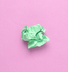 Green crumpled sheet of paper on light pink background. Minimal still life