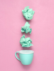 Blue crumpled sheet of paper with cup on pink background. Minimal still life