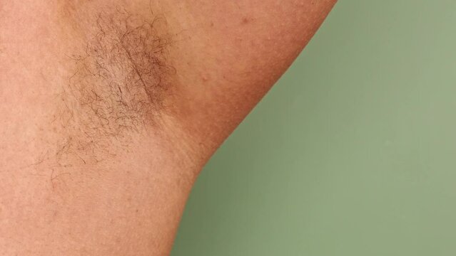 Close-up demonstration of woman's unshaven armpit. Laser depilation. Body positive. Hygiene and self-care. Choice of skin care products. Green background. Skin sensitivity testing. 4k footage.