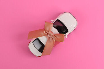 Toy auto model rewound gift ribbon with bow on pink background. Car as gift, surprise