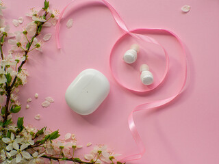 White wireless headphones on pink background with cherry flowers. Womens, Valentines and Mothers Day gift. Concept of music, spring and elegance. Buying birthday gifts. 