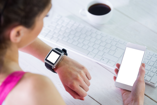 Woman holding mobile phone while sitting by keyboard on table at home