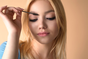 Beautiful woman applies brow gel with brows brush to her eyebrow. Studio portrait of young woman doing her eyebrow natural make up. Eyebrows make up concept.