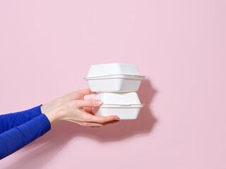 Female hand holding food container for takeaway burger. Flash light, copy space