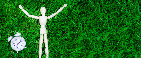 Time for rest, freedom concept. The figure of a man and an alarm clock on the green grass. Banner, place for text.