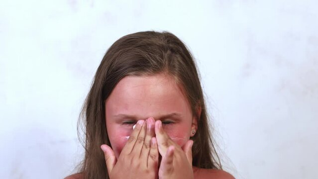 Portrait of serious little girl applying smoothing panthenol healing cream on burnt reddened skin on face on white background. Skin care, UV protection, sunburn, sunscreen, sun block, moisturizing.