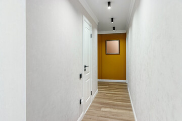 White door to the room at the end of a long corridor with a yellow wall and a painting