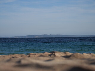Obraz premium Traumblick vom Sandstrand auf das blaue Meer, im Hintergrund eine Insel