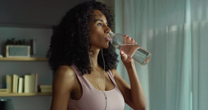 Portrait of Strong Southeast Asian Fitness Girl in Workout Clothes Taking a Break from Exercising at Home to Drink Water. Female Fitness Enthusiast Training, Working on her Stamina. Slow Motion