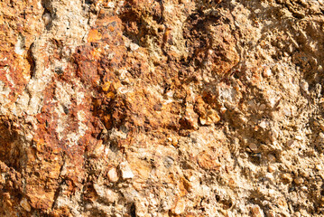 Sand-colored stone wall in the rays of the sun. Rough and uneven surface.
