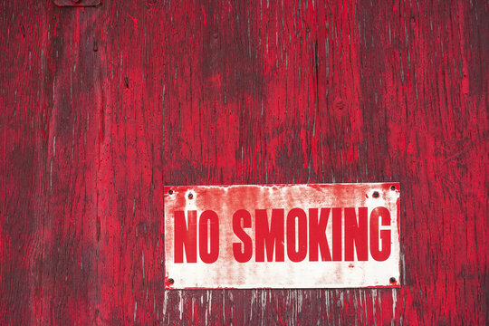 A No Smoking Sign On A Painted Red Wooden Wall; Orion, Alberta, Canada