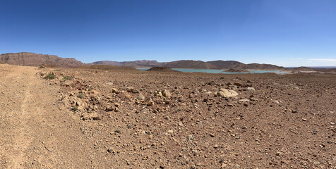 Morocco, Africa: panoramic dirt road and with on the background the view of Barrage Al-Hassan Addakhil, a light blue lake in the valley of the Ziz, in the High Atlas Mountains region 
