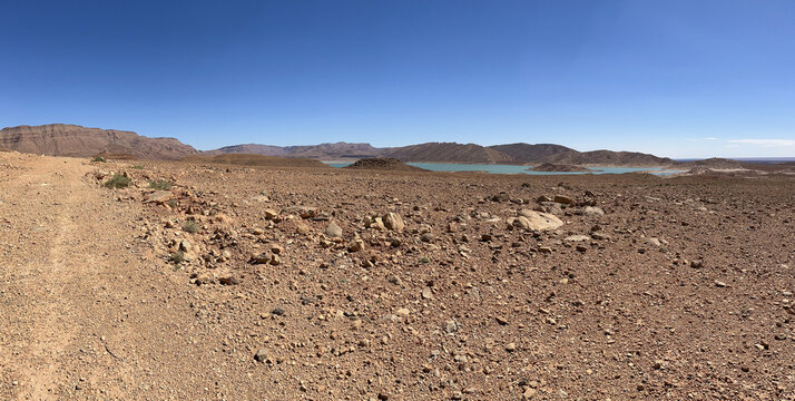 Morocco, Africa: panoramic dirt road and with on the background the view of Barrage Al-Hassan Addakhil, a light blue lake in the valley of the Ziz, in the High Atlas Mountains region 