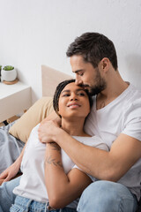 Fototapeta premium bearded man hugging young and happy african american woman smiling on bed at home.