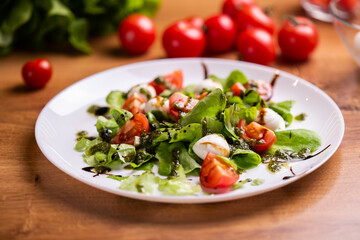 Plate of healthy classic close-up caprese salad with mozzarella cheese tomatoes and basil in kitchen - italian cuisine