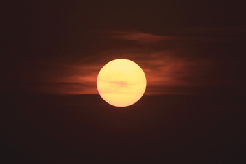 A glowing yellow sun sinking in a dark sky with red clouds; Lake of the Woods, Ontario, Canada