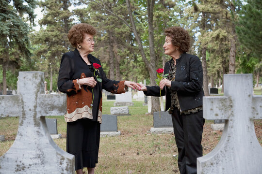 Two Women Holding Single Red Roses At A Grave In A Cemetery; Edmonton, Alberta, Canada