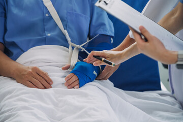 Injured patient showing doctor broken wrist and arm with bandage in hospital office or emergency room. Sprain, stress fracture or repetitive strain injury in hand. Nurse helping customer. First aid.