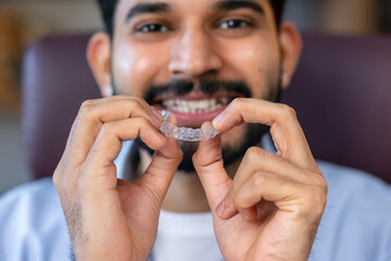Man showing an invisible silicone aligner for dental correction. Male hands holding the plastic braces dentistry retainers to straighten teeth
