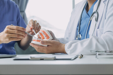 Dentists are discussing dental problems at report x-ray image on laptop screen to patients.