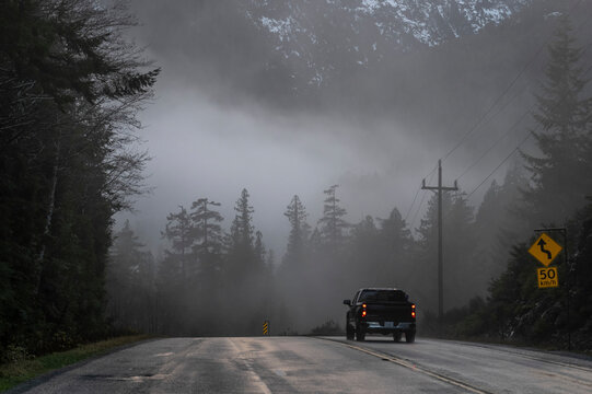 A pickup truck drives along a road into a fog bank covering the road and forest ahead on Vancouver Island; Alberni-Clayoquot Regional District, British Columbia, Canada