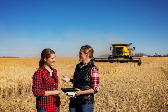 Woman farmer teaching apprentice advanced farming technologies during grain harvest, Alberta, Canada