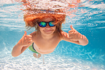 Fototapeta premium Child in swimming in pool. Funny little boy swims underwater in the pool. Underwater kids portrait from under the water. Summer holiday. Kids weekend.