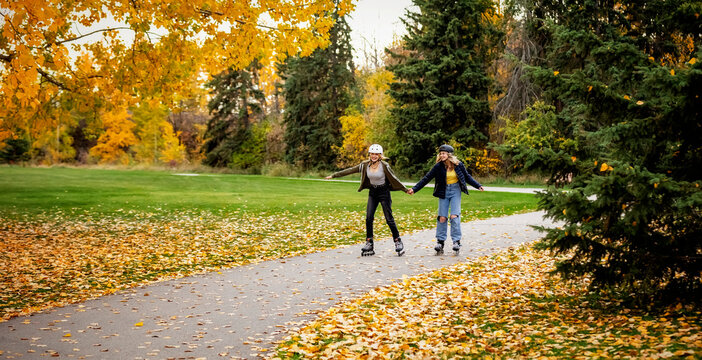 Two teenagers rollerblading together in a city park during a warm fall afternoon; St. Albert, Alberta, Canada