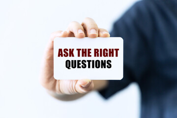 Ask the right questions text on blank business card being held by a woman's hand with blurred background. Business concept about asking the right questions.