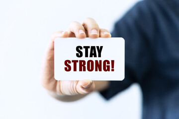 Stay strong text on blank business card being held by a woman's hand with blurred background. Business concept about stay strong.