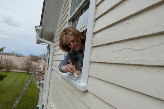 Woman carefully paints a windowsill of a restored farmhouse; Walton, Nebraska, United States of America