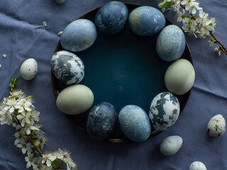 Blue painted easter eggs. Dyed Easter eggs with marble stone effect blue color on blue tablecloth background with cherry blossom twigs. Eggs background with copy space, Ester holiday postcard concept.