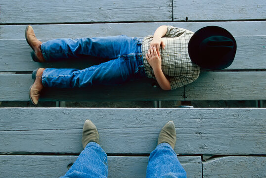 Young cowboy has a nap on the grandstands, face covered by a hat and a pair of clad feet; Burwell, Nebraska, United States of America