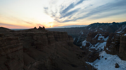 Charyn Grand Canyon with orange rock walls. Aerial view from the drone of the steep canyon walls, cracks and tunnels. There is snow in places. Beautiful sunset and sunrise. Brother of the Grand Canyon