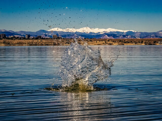 Water splash created by rock thrown into lake, snow-capped peaks in the background