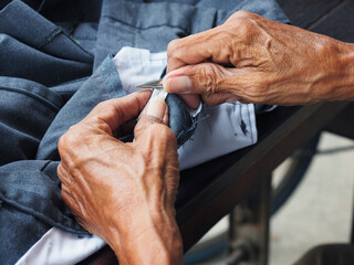 Elderly man hands fixing the pant and cutting the thread on the sewing machine close-up.