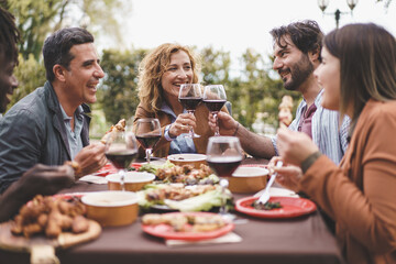 Friends Enjoying Outdoor Dinner - A group of friends aged 25-45 enjoying skewers and wine in the garden. A bearded man and a mature blonde woman toast during a pleasant summer evening.