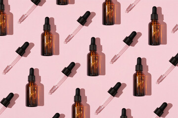 Simple face skincare pattern made with dark brown glass serum or essential oil bottle and dropper on pastel pink background. Minimal fresh product aesthetic.