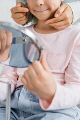 Cropped view of speech therapist pointing at cheek of pupil with mirror in consulting room.
