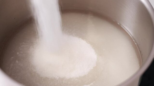 Close up of sugar being screwed into steel saucepan with water on the bottom for syrup to melt it on the fire and make homemade caramel, meringue, lollipops. ingredients for desserts for pastry shop.