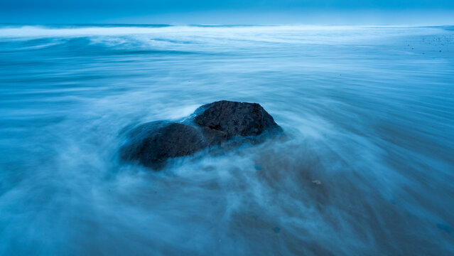 Surf swirling around a rock by the shore at dawn on Marconi Beach; Welfleet, Massachusetts, United States of America