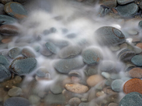 Blurred seawater washes over beach pebbles; Greymouth, South Island, New Zealand
