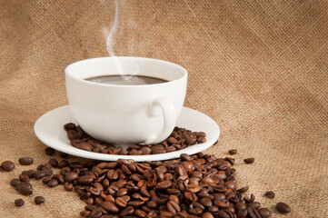 Cup of coffee on a saucer with coffee beans on a background of burlap